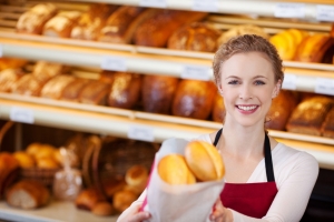 Portrait of happy female worker giving bag of breads in bakery